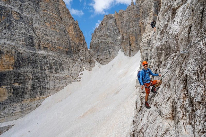 Mountaineer climbs on a steep rock face in the Via Ferrata Brentari via ferrata, spectacular mountain landscape with steep rock faces, remains of the Vedretta d'Ambiez glacier in the back, Brenta Mountains, Brenta-Adamello Nature Park, Trentino, Italy