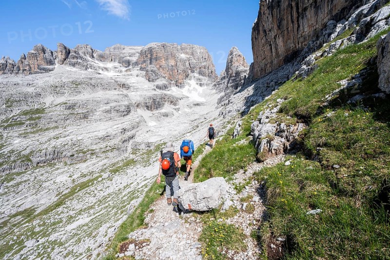 Three mountaineers on a hiking trail to Sella della Tosa, mountainous landscape in the Brenta Mountains, Brenta-Adamello Natural Park, Trentino, Italy