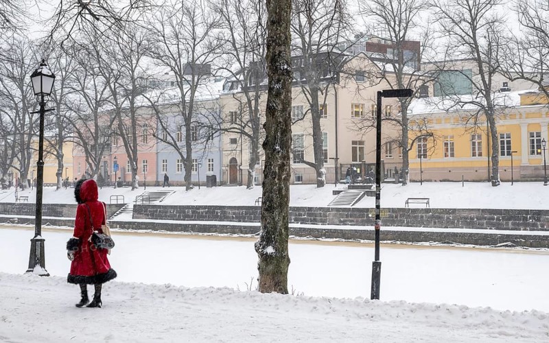 Woman in red winter coat walks along the frozen Aurajoki river, wintery Turku or Swedish Åbo, Varsinais-Suomi, Finland