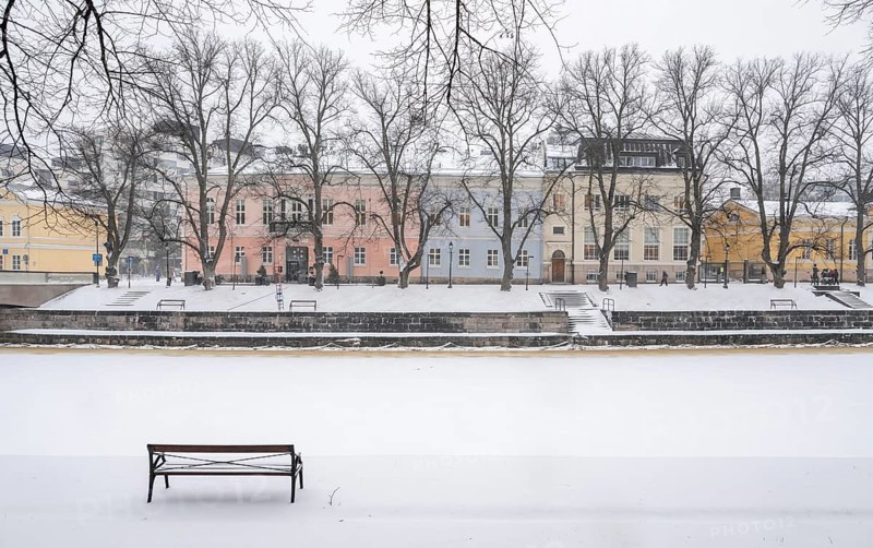 Bench, historic buildings on the frozen Aurajoki River, wintery Turku or Swedish Åbo, Varsinais-Suomi, Finland