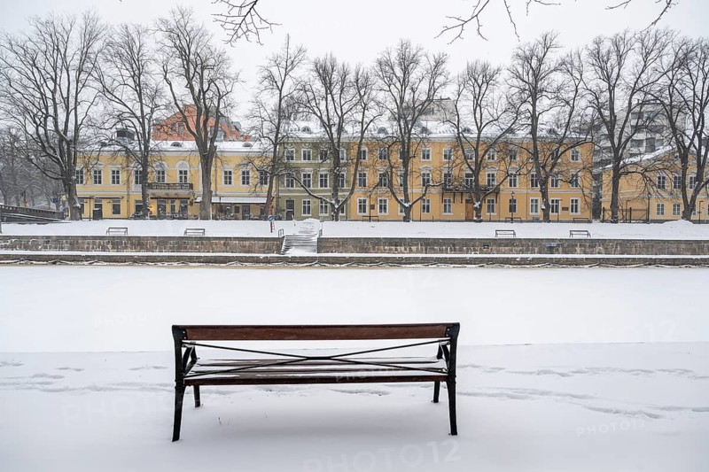 Bench and historic buildings on the frozen Aurajoki river, wintery Turku or Swedish Åbo, Varsinais-Suomi, Finland