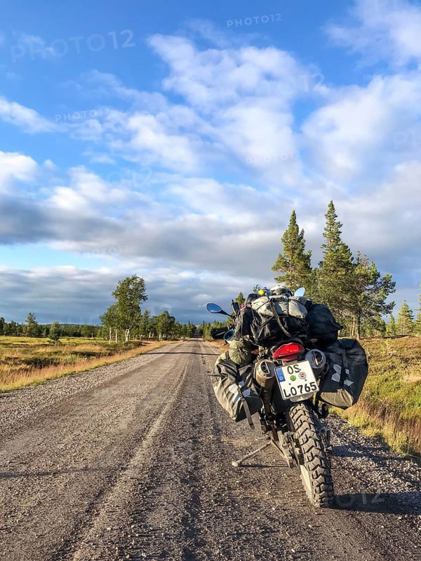 Idre, Dalarnas län, Sweden, BMW G 650 GS Sertao enduro motorcycle with complete camping equipment stands on a gravel road with blue sky and evening light