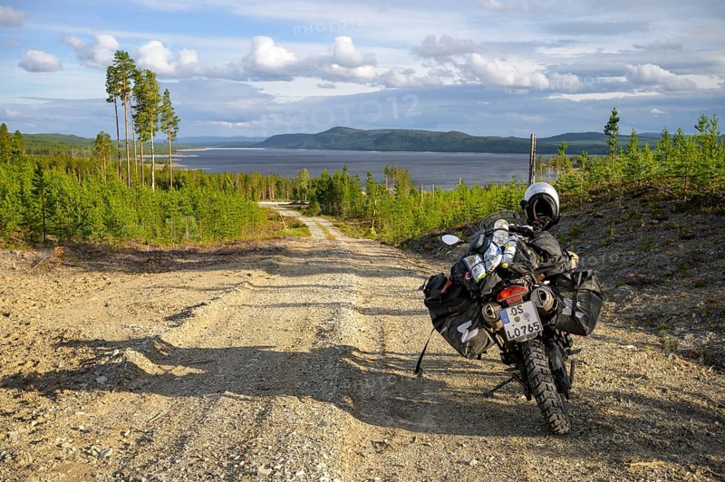 Lövdalen, Jämtland County, Sweden, A dirt road leads through slightly wooded terrain with a BMW G 650 GS Sertao enduro motorcycle and lake in the background