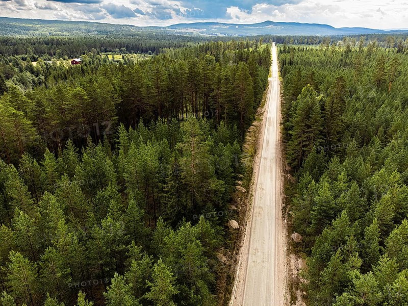 Torsby, Värmlands län, Sweden, Long road through a thick green forest under a wide, cloudy sky, aerial view
