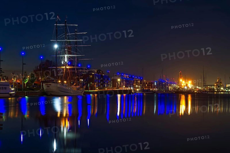 Nocturnal harbor with illuminated sailing ship and reflections in calm water
