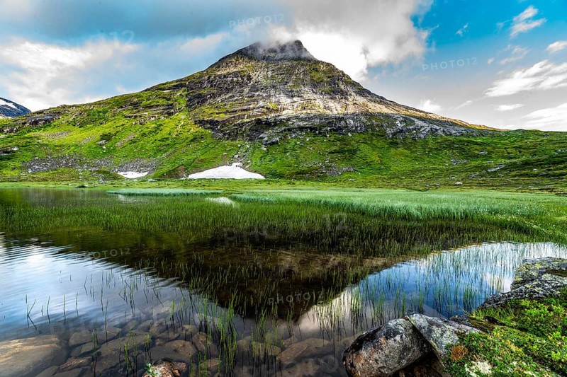 Mountain lake with mirror-like water and green slopes, peaceful and calm under a blue sky