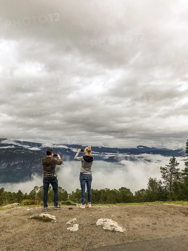 Utvik, Vestland, Norway, Two people photograph a foggy landscape with mountains and clouds with their smartphones