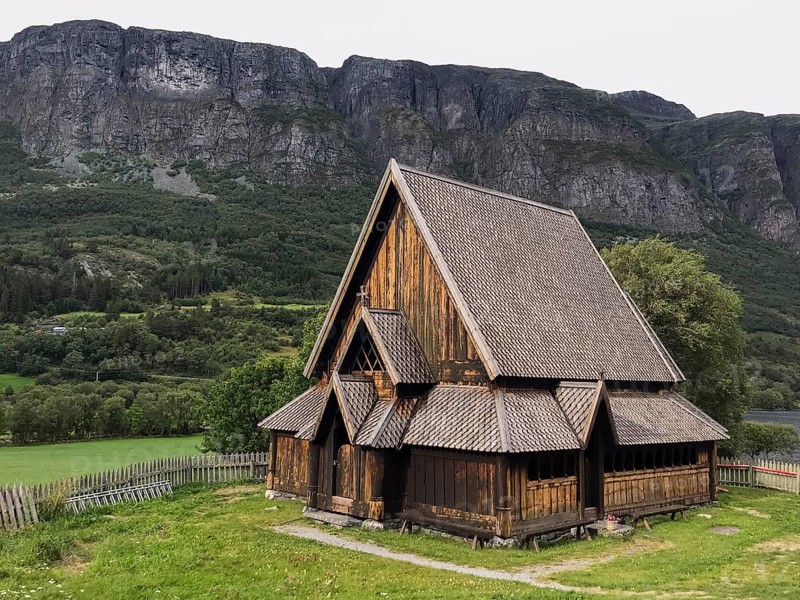 Øye, Innlandet, Norway, Traditional stave church in front of steep mountains in rural surroundings, traditional wooden church in front of impressive mountain cliffs in a quiet landscape