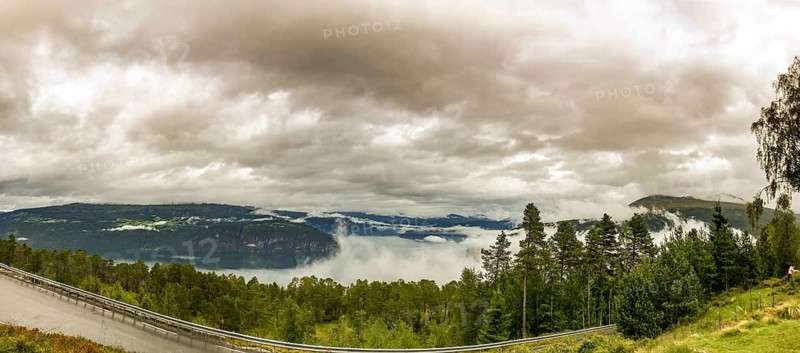Utvik, Vestland, Norway, panoramic view of foggy mountain slopes and a dense forest under cloudy sky, wide view of a foggy landscape with forest and lake under a cloudy sky