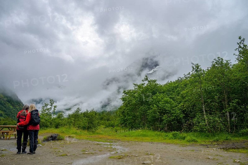 Fjærland, Vestland, Norway, couple looking at misty mountains surrounded by thick forest and a cloudy sky