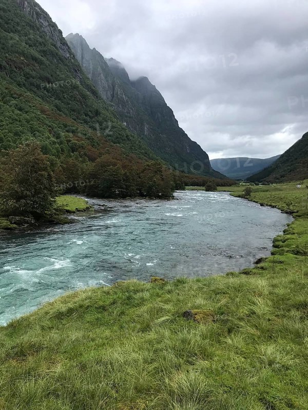 Byrkjelo, Vestland, Norway, river flows through a valley surrounded by green meadows and thick forests, A calm river flowing through a green, mountainous landscape under cloudy skies