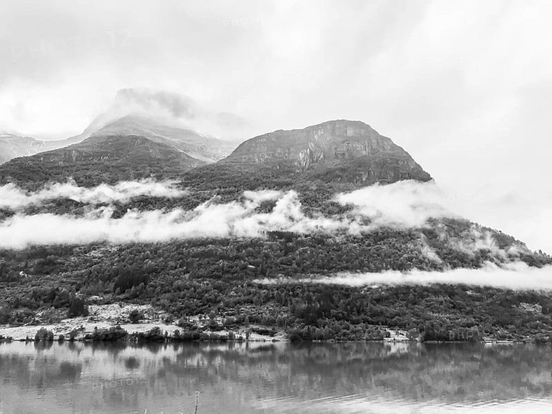 Olden, Vestland, Norway, black and white landscape of mountains with low-hanging clouds and reflecting water near Brikdalsbreen glacier