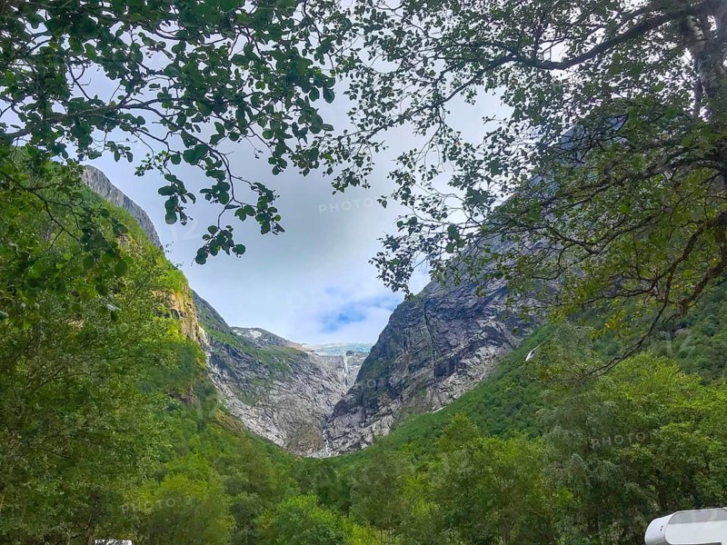 Oldedalen, Vestland, Norway, view through trees of an impressive mountain gorge under a calm sky of the Brikdalsbreen glacier