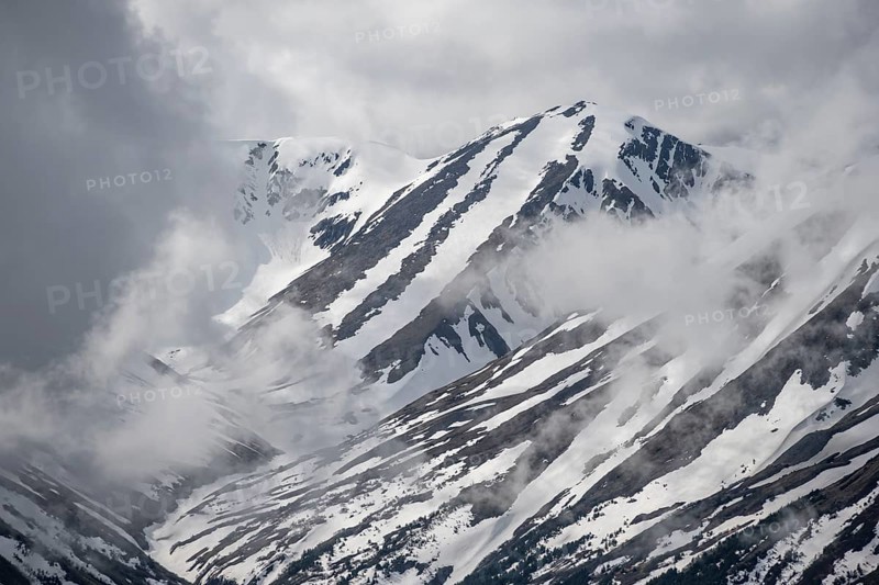 Fog sweeps around mountain peaks with remnants of snow, view from Slaughter Ridge Trail, Cooper Landing, Kenai Peninsula, Alaska, USA