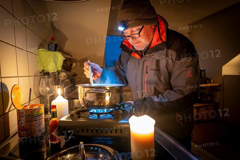 Symbolic picture blackout, extensive, prolonged power failure, in private settings, without electricity, heating, water, cooking in the kitchen, heating food with a gas-powered camping stove, which is also approved for indoor use