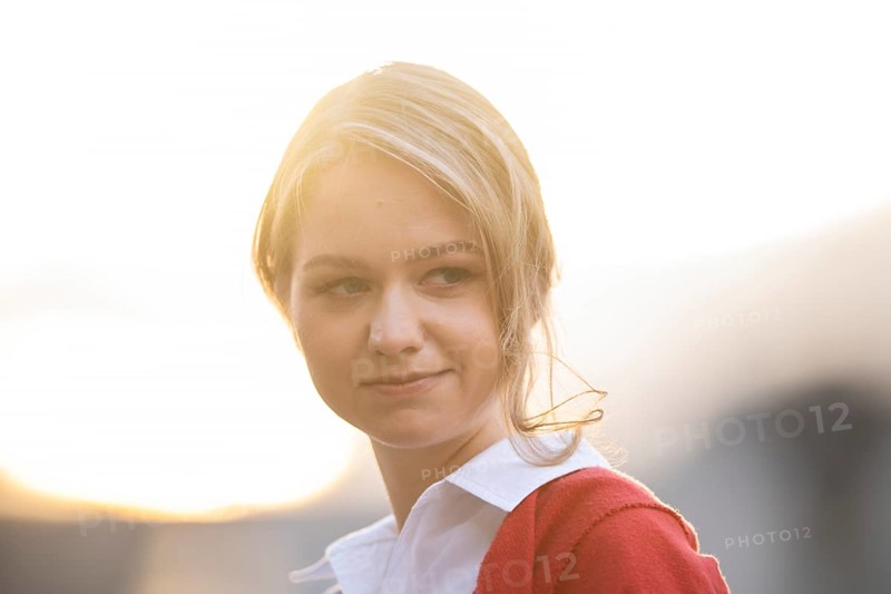 Serious looking young woman in white blouse and red cardigan, in backlight, Stuttgart, Baden-Württemberg, Germany