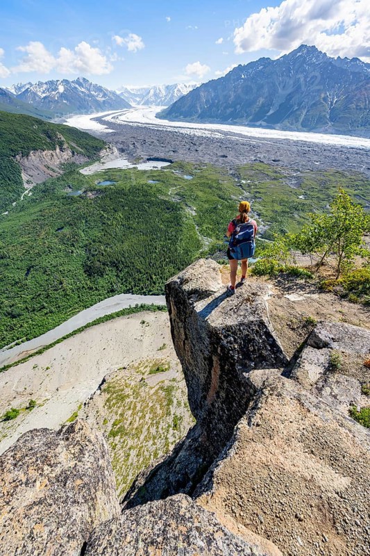 Young woman on a rocky outcrop enjoying the view, view of impressive mountain landscape with Matanuska glacier and glaciated mountain peaks, Lion's Head, Chugach Mountains, Alaska, USA