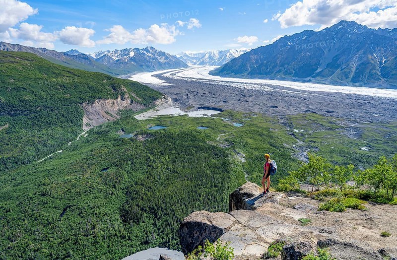 Young woman on a rocky outcrop enjoying the view, view of impressive mountain landscape with Matanuska glacier and glaciated mountain peaks, Lion's Head, Chugach Mountains, Alaska, USA
