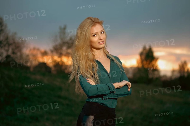 Cheerful woman with blonde hair stands with her arms crossed on a heel during sunset. Retreat in a calm environment