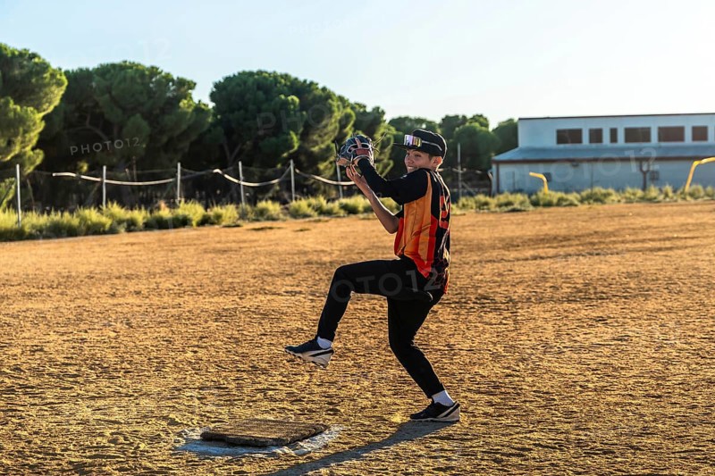 Boy pitching on a dusty baseball field in uniform and sport glasses, smiling as he throws a fast pitch on a sunny afternoon, focused and enjoying youth baseball