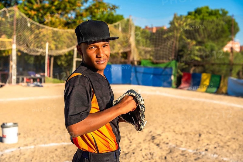 Confident young baseball player stands on dusty field gripping his glove, smiling at the camera and ready for the game, showcasing focus, dedication and outdoor athletic spirit