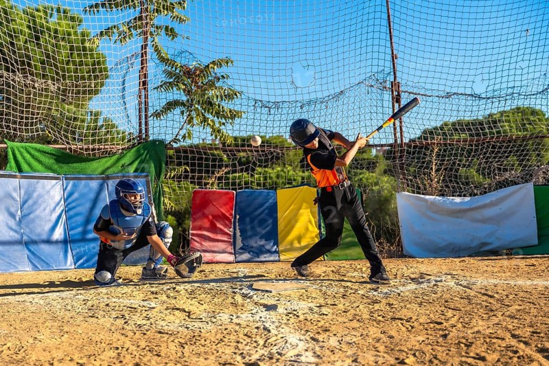 Young baseball players honing their skills, with a batter swinging a bat to hit a flying ball and a catcher ready behind home plate during an outdoor practice session