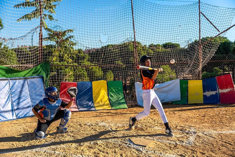 Young baseball players focusing on sport, with a batter hitting a baseball and a catcher ready behind the plate during an outdoor practice session, demonstrating youth sports engagement