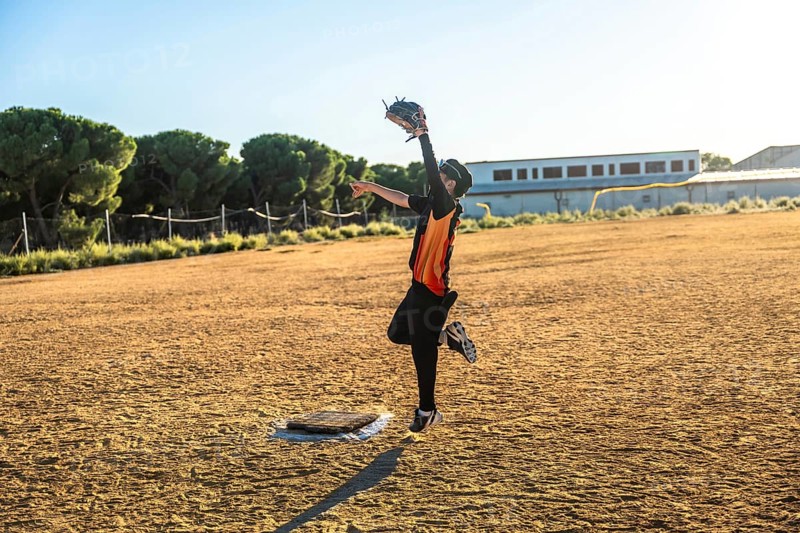 Young baseball player in uniform and glove jumping to catch a flying ball on a sunny dirt field, demonstrating effort, action, and determination in sport
