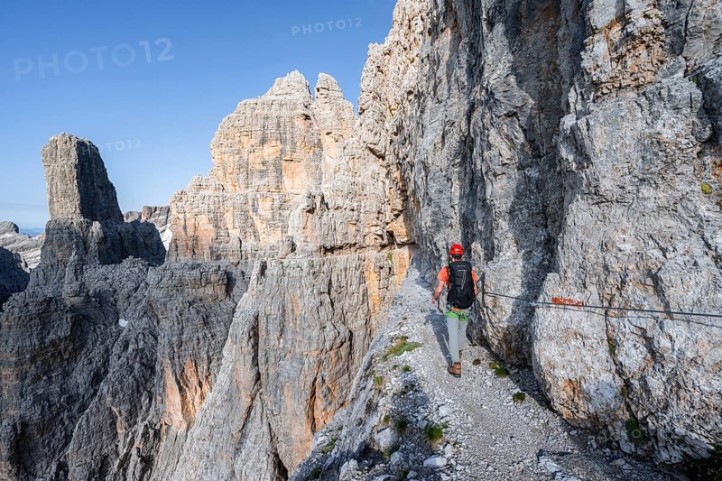 Mountaineers on an exposed rock band in the secured Via Ferrata Bocciere Centrale via ferrata, spectacular mountain landscape with steep rocky peaks, Brenta-Adamello Nature Park, Trentino, Italy