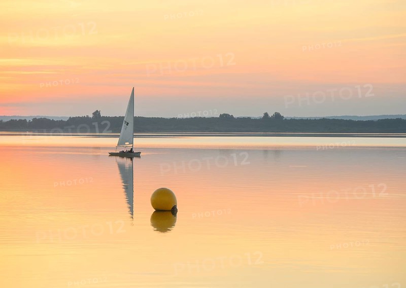 Sailing boat glides on quiet Dümmer Lake with a yellow buoy at sunset, Dümmer nature park Park, Lower Saxony, Germany