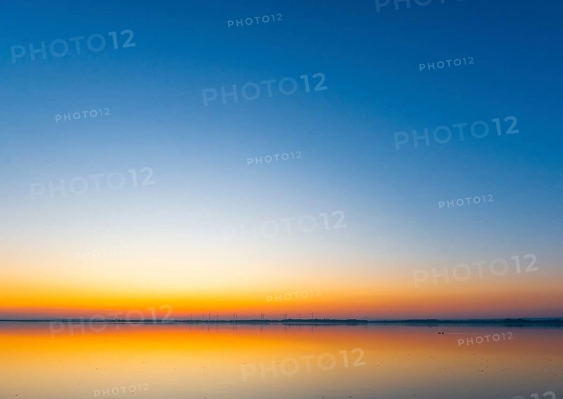 A calm sunrise with a soft color gradient is reflected in the still water of Lake Ddümmer, Dümmer nature park Park, Lower Saxony, Germany