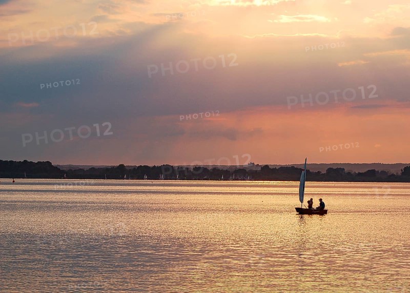 Two children 6 and 10 years old in a small red sailboat Optimist Jolle Opti on the Dümmer at golden evening light, Dümmer nature park Park, Lembruch, Lower Saxony, Germany