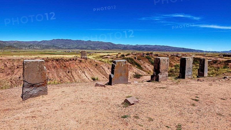 Standing stone monoliths overlook a vast open area with mountain backdrop, the archaeological site with the ruins of Tiwanaku in Bolivia