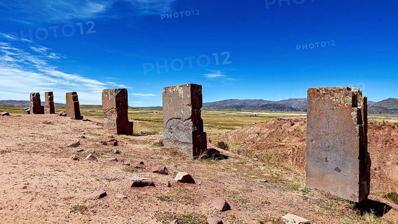 Row of standing stone monoliths along an open area with mountains in the background, the archaeological site with the ruins of Tiwanaku in Bolivia