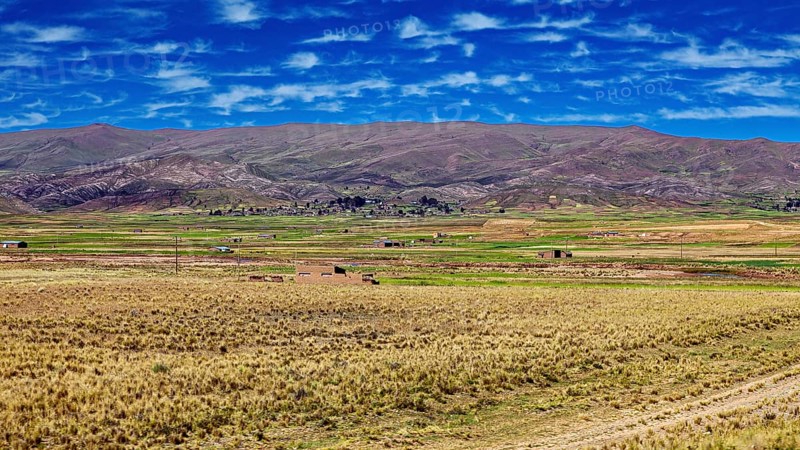 Wide fields against mountains and cloudy blue sky, The Altiplano landscape in the Andes of Bolivia