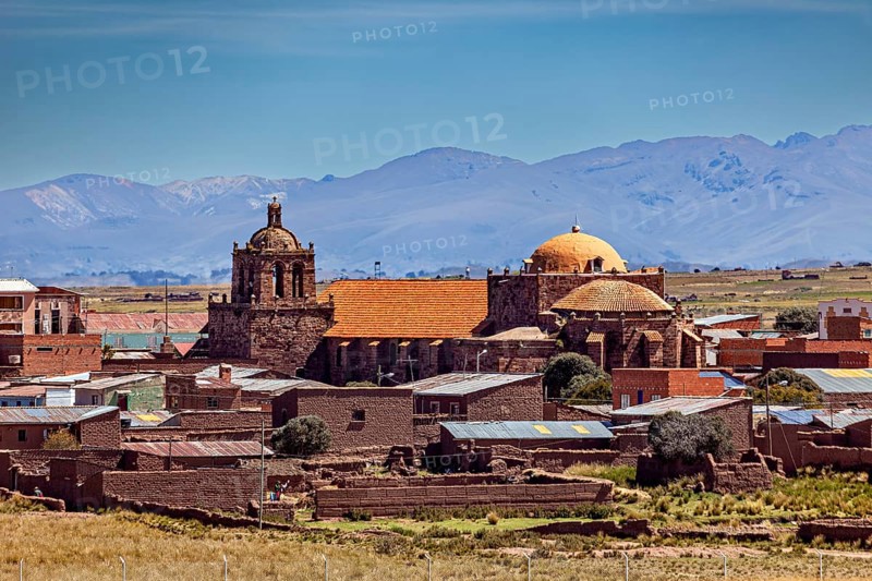 Historic church in a village with brick red roofs against a mountain backdrop under clear skies, The city of Tiwanaku near the ruins of Tiwanaku in Bolivia