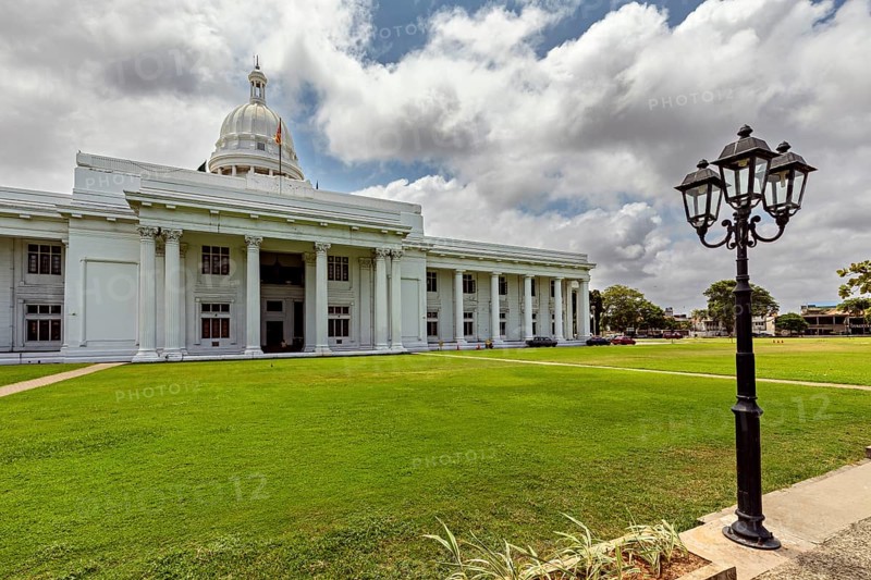 A white building with dome and pillars surrounded by green lawn under cloudy sky, Colombo Sri Lanka City Council