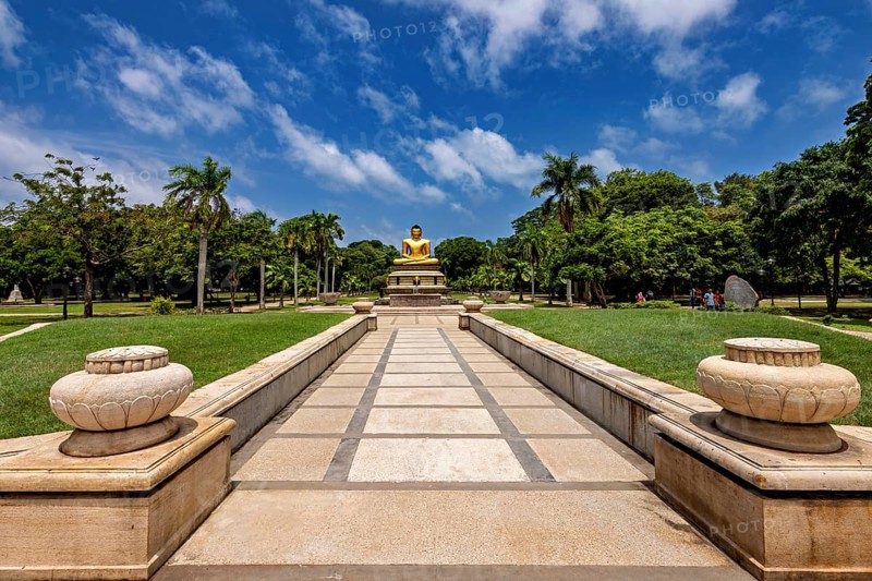 Quiet park with centrally placed Buddha statue and stone path under blue sky, The Golden Buddha in Colombo Sri Lanka City Park