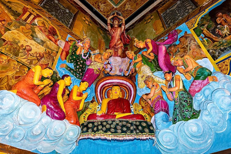 Buddha scene with figures standing in prayer surrounded by colorful frescoes and vivid colors, The Gangaramaya Temple with the Buddha statues in Colombo Sri Lanka