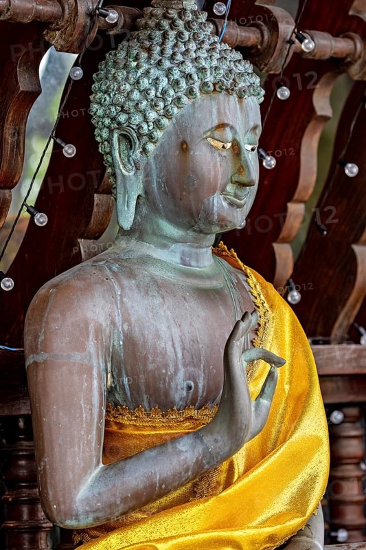 Close-up of a Buddha statue in bronze with a bright yellow cloth, The Seema Malaka temple with the Buddha statues in Colombo Sri Lanka