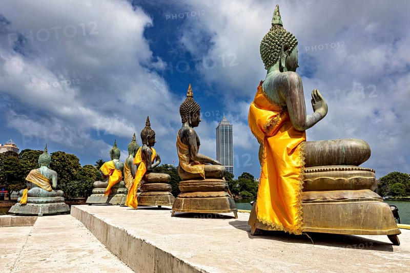 Buddha statues on the water with yellow robes against an urban backdrop, The Seema Malaka Temple with the Buddha statues in Colombo Sri Lanka