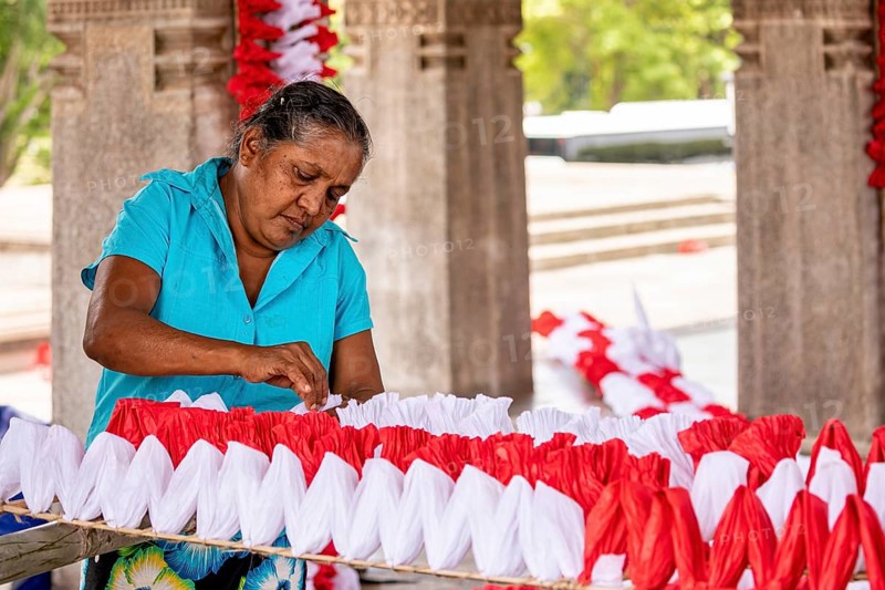 Woman making red and white decorations in an enclosed space, people making garlands in Colombo Sri Lanka City Hall