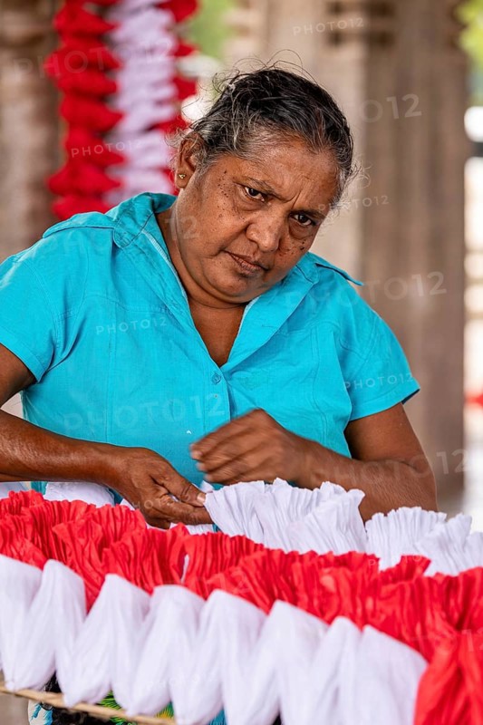 Woman concentrates making red and white decorations, people making garlands in Colombo Sri Lanka City Hall