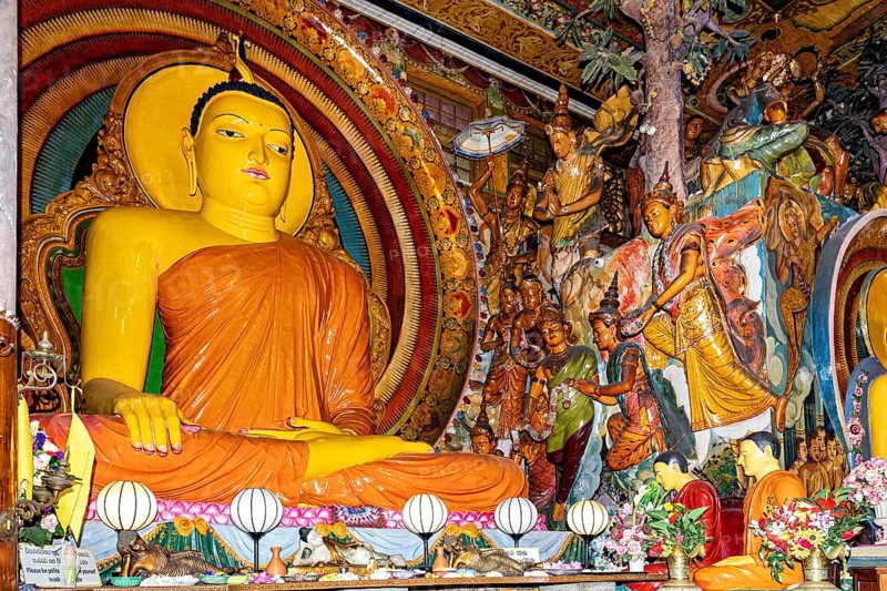 Buddha statue on an altar surrounded by frescoes and religious figures in a spiritual and colorful scene, The Gangaramaya Temple with the Buddha statues in Colombo Sri Lanka