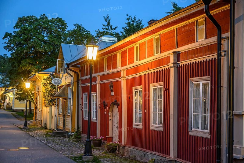 Street scene in the old town of Naantali, red historic wooden building with decorative windows on a paved street in the evening light with cozy street lighting, Naanatali, Varsinais-Suomi, Finland