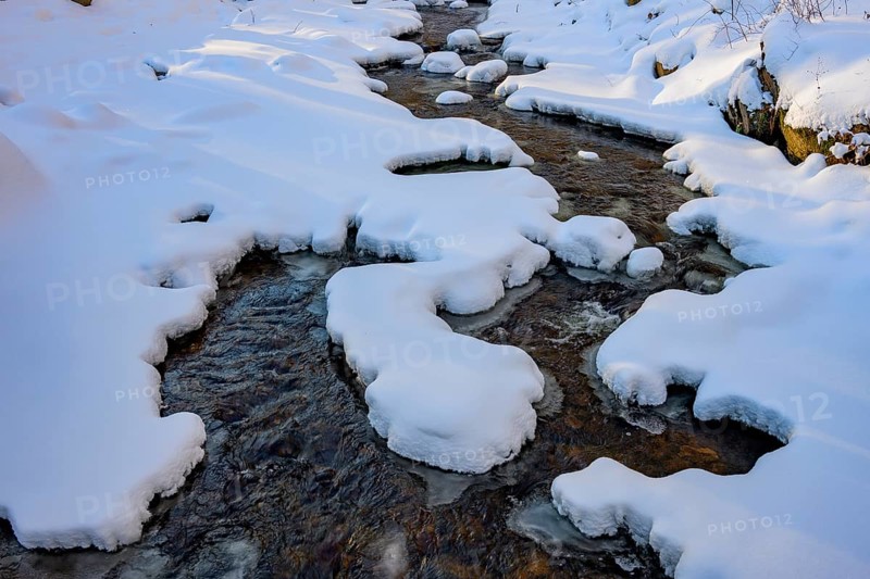 Ilsenburg, Saxony-Anhalt, Germany, A stream flows through a snow-covered landscape with layers of ice on the Ilse river in the Harz National Park on the Heinrich-Heine trail Ilsetal hiking trail