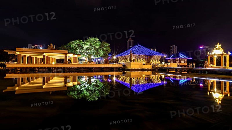 Nocturnal scene with illuminated pavilions, reflections in the water and city in the background, The Seema Malaka Temple with the Buddha Statues in Colombo Sri Lanka