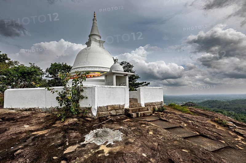 White stupa on rocky hill surrounded by cloudy skies and lush nature, The Maligatenna Purana Rajamaha Viharaya monastery near Colombo Sri Lanka