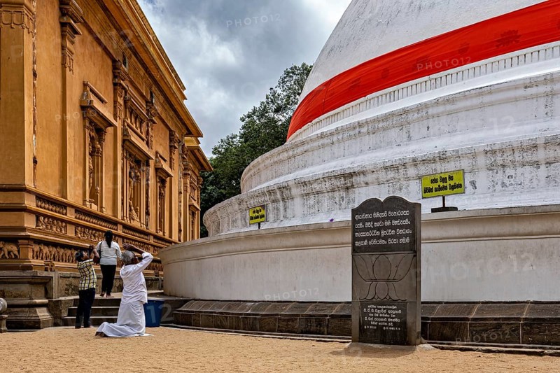 Pilgrims wearing white clothes pray in front of a large vault with religious inscription under cloudy sky, The Kelaniya Temple in Colombo Sri Lanka
