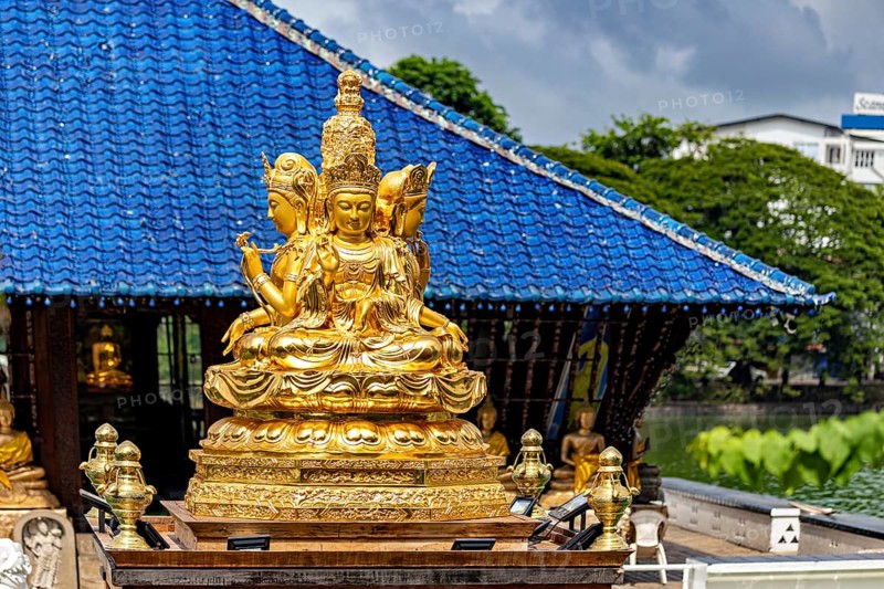 Golden Buddhist statue in front of a blue roof with cloudy sky, The Seema Malaka Temple with the Buddha Statues in Colombo Sri Lanka